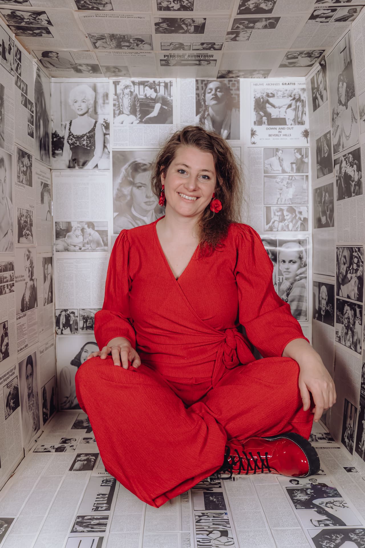 Mieke in een rode jurk, zittend tussen oude filmposters